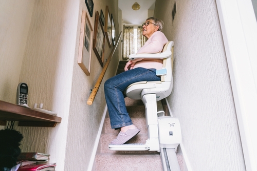 An older woman sits on a chair lift in her home.