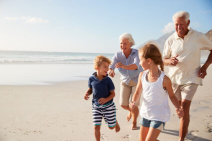 Two grandparents run along the beach playing with their grandkids.