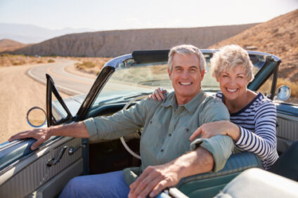 An older couple smiles as they sit in a classic car.