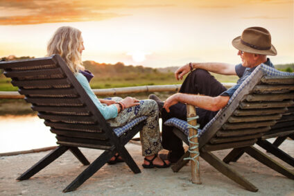 An older couple sits on beach chairs facing the sunset.