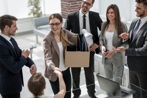 A young businesswoman greets her new coworkers while holding a moving box.
