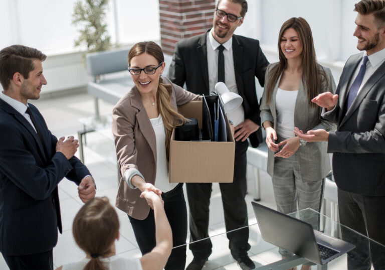 A young businesswoman greets her new coworkers while holding a moving box.