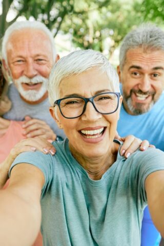 A group of older adults smiles for a selfie while standing in a park.