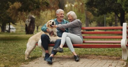 An older couple plays with their dog on a park bench.