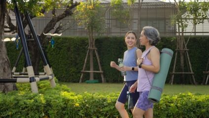 An older woman and a younger woman walk in a park while carrying yoga mats.