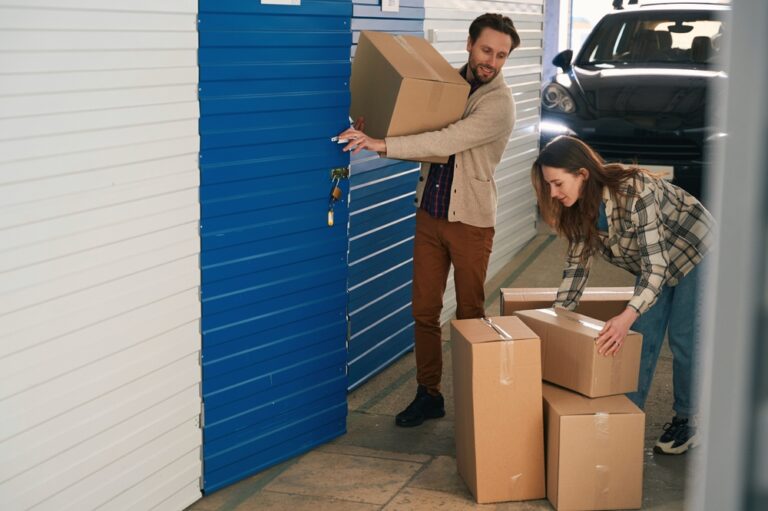 A couple moves cardboard boxes into a storage unit.