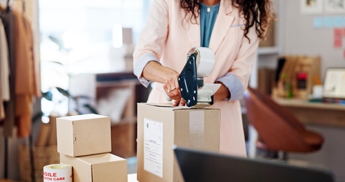 A woman tapes up a box in an office.